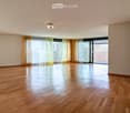 Empty room with wooden flooring, large windows with curtains, and a sliding glass door leading to a balcony.
