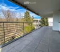 Balcony with tiled floor, metal railing, and a view of trees and a building in the background.