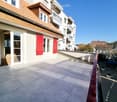 Balcony with tiled floor, red railing, and view of neighboring buildings and a parked car.