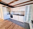 Modern kitchen with white cabinets, stainless steel appliances, wooden flooring, and a black countertop.