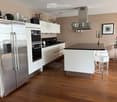 Modern kitchen with white cabinets, stainless steel appliances, wooden flooring, and a central island with bar stools.