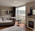 Modern living room with a patterned sofa, a small round coffee table, a decorative fireplace with an electric fire, and large windows with a balcony view.