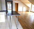 Modern kitchen with a black countertop table, white cabinets, and wooden flooring. The room features large windows and a door leading to a balcony.