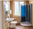Modern bathroom with a white sink, toilet, and a glass-enclosed shower stall. The walls are decorated with floral wallpaper, and the floor is tiled in brown.