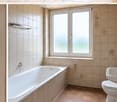 Bathroom with beige tiles, a bathtub, a sink, a toilet, and a window with frosted glass. The walls have decorative floral tiles, and there is a mirror above the sink.