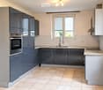 Modern kitchen with grey cabinets, stainless steel oven, sink, and countertop. Natural light from a window above the sink.