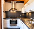 Modern kitchen with white cabinets, stainless steel appliances, dark countertops, and a sleek range hood.