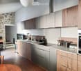 Modern kitchen with wooden cabinets, stainless steel countertops, induction stove, sink, oven, toaster, trash bin, chandelier