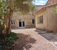 Courtyard with stone building, paved courtyard, stairs, wooden bench, plants, and small table.