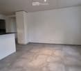 Empty kitchen with white cabinets, a black countertop, and a large window letting in natural light. The floor is tiled, and the space is clean and uncluttered.