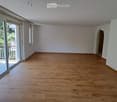 Empty room with wooden flooring, white walls, large sliding glass doors leading to a balcony, and a small arched doorway.