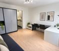 Modern, well-lit room with a sofa, desk, and cabinet. Features a light wooden floor, white walls, and decorative plants.
