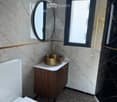 Modern bathroom with marble walls, a white toilet, a gold sink, a round mirror, and a wooden cabinet.