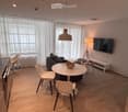 Modern living room with a sofa, round table, chairs, a hanging lamp, a floor lamp, a TV screen, and a small stool.