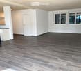 Empty room with dark wooden flooring, white walls, and large windows. No furniture or equipment present.