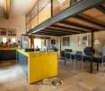 Open-plan kitchen and dining area with a yellow kitchen island, stainless steel appliances, dining table with chairs, and various kitchen items on counters.