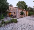 A rustic stone house with a gravel courtyard, outdoor seating, and greenery.