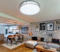 Modern open-plan living and dining area with a grey sofa, wooden coffee table, dining table with chairs, and a cat tree. The space features a sleek kitchen area with white cabinets and stainless steel appliances, complemented by framed artwork on the wall
