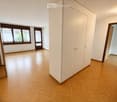 Empty room with wooden flooring, white walls, large window with curtains, and a tall white wardrobe. No furniture or personal items present.