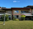 A two-story house with a well-maintained lawn, multiple windows, and a covered patio area with outdoor furniture.