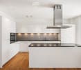 Modern kitchen with white cabinets, black countertops, and a central island. Features include an oven, sink, range hood, and ample storage space.