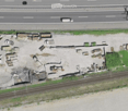 Aerial view of a construction site with scattered materials, partially built structures, and a nearby road and railway tracks.