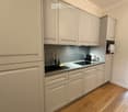 Modern kitchen with light-colored cabinets, a sink, a faucet, an oven, and a microwave. The countertops are clean and the floor is made of light wood.