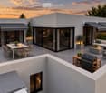 Modern rooftop terrace with a dining area, lounge seating, barbecue, and potted plants, overlooking a scenic sunset view.