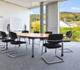 Modern conference room with a large wooden table, black chairs, and a large screen, overlooking a scenic landscape.