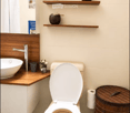 Modern bathroom with a white toilet, wooden shelf, sink, and decorative items.