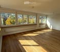 Empty room with wooden flooring, large windows, and radiators. No furniture or equipment present.