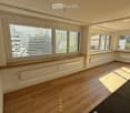 Empty room with wooden flooring, large windows with blinds, and radiators beneath the windows.