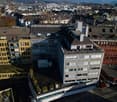 Aerial view of a multi-story building with a flat roof and surrounding structures in an urban setting.