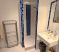 Modern bathroom with white tiles, blue mosaic accents, bathtub, sink, mirror, towel rack, and small trash bin.