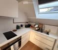 Compact kitchen with white cabinets, a black induction cooktop, and a stainless steel sink. The countertop holds various kitchen items including a blender, toaster, cups, and bottles.