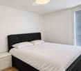 Modern bedroom with a double bed, white bedding, a nightstand, and a large window with blinds.