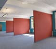 Empty room with grey carpet, white and teal walls, two windows, and a door leading to another space.