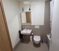 Modern bathroom with a white sink, toilet, mirror, and tiled walls. Includes a towel, toilet paper, and a shower curtain.