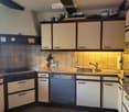 The kitchen features light-colored cabinets, a stainless steel dishwasher, a sink with a faucet, and various kitchen items on the countertops.