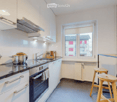 Modern kitchen with white cabinets, stainless steel appliances, a stove, oven, sink, and a small table with stools.