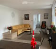 Bright living room with a yellow sofa, coffee table, side table, piano, and decorative items including a teddy bear and a small red elf figure.