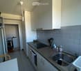 Modern kitchen with white cabinets, granite countertop, stainless steel sink, and built-in oven. Visible items include a dish rack, kitchen utensils, and a refrigerator in the background.