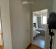 A narrow hallway with wooden flooring leads to a bathroom. The bathroom features a toilet, sink, bathtub, and tiled walls.