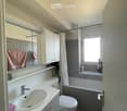 Modern bathroom with a sink, mirror, cabinet, toilet, bathtub, and window. Features a pink towel on the sink and a small plant on the windowsill.