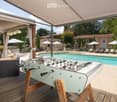 Outdoor area with a swimming pool, covered seating area, foosball table, lounge chairs, and umbrellas.