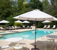A spacious outdoor area featuring a swimming pool surrounded by lounge chairs, umbrellas, and a dining set with a table and chairs.