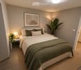 Modern bedroom with a neatly made bed, nightstand, table lamp, and decorative plants. The room features a large picture frame on the wall and warm lighting.