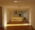 Empty hallway with wooden floor, white walls, kitchen with cabinets, sink, and oven, and a ceiling light.