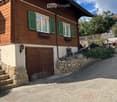 Two-story wooden house with green shutters, a garage, and a stone pathway leading to the entrance.
