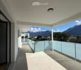 Modern balcony with light-colored tiled flooring, glass railings, and a scenic mountain view in the background.